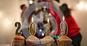 New Year celebration. Cupcakes with candles in numbers 2019 stand on the table before a cheerful company celebrating New