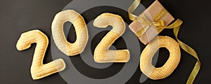 New Year celebration and festive background with yellow numbers 2020, and craft gift box decorated golden ribbon and bow on black