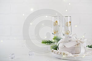 New Year Celebration. Silver Christmas table setting with two champagne glasses on the dinner table and gift box.