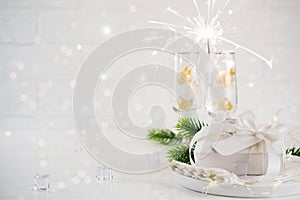 New Year Celebration. Silver Christmas table setting with two champagne glasses on the dinner table and gift box.