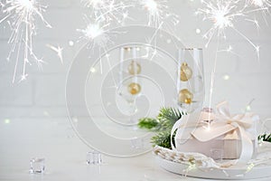 New Year Celebration. Silver Christmas table setting with two champagne glasses on the dinner table and gift box.