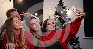 New Year celebration. Two young couples taker a selfie on the smartphone sitting before a Christmas tree