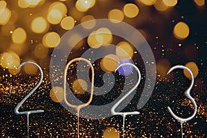 New Year, Christmas background. Candle numbers 2023 in silver and golden on a back background with lights and glitter