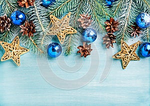 New Year or Christmas background: fir branches, blue glass balls, cones, golden stars over turquoise wooden backdrop