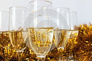 Glasses with champagne with gold tinsel on light gray background. New year or Christmas concept.