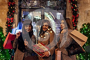 New Year, Christmas concept. Women friends holding shopping bags with presents in Lviv by decorated stores on street.