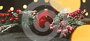 New Year and Christmas decoration, holiday background. Red festive ball bauble, green fir xmas tree and yellow blurred lights.