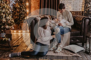 New Year. Christmas. Family. Young parents and their little daughter in Santa hats are spending time together near the Xmas tree