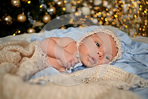 New Year Christmas holidays scene - cute newborn baby boy in funny hat lying on knitted beige blanket with Christmas