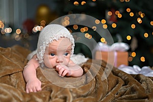 New Year Christmas holidays scene - cute newborn baby boy in funny hat lying on knitted beige blanket with Christmas