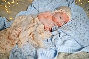 New Year Christmas holidays scene - cute newborn baby boy in funny hat lying on knitted beige blanket with Christmas