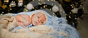 New Year Christmas holidays scene - cute newborn baby boy in funny hat lying on knitted beige blanket with Christmas