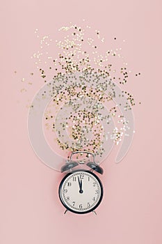 New Year Christmas Top view flat lay black alarm clock twelve covered golden stars confetti copy space millennial pink color paper