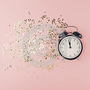 New Year Christmas Top view flat lay black alarm clock twelve covered golden stars confetti copy space millennial pink color paper