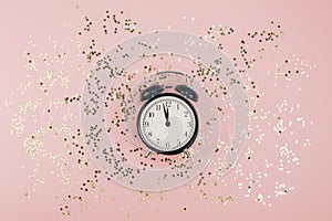 New Year Christmas Top view flat lay black alarm clock twelve covered golden stars confetti copy space millennial pink color paper