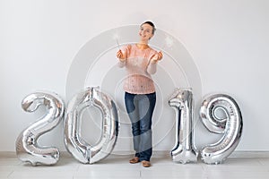 New 2019 Year is coming concept - Happy woman standing near silver colored numbers and sparklers indoors.