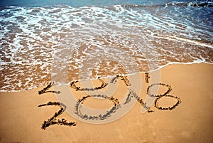 New Year 2018 is coming concept - inscription 2017 and 2018 on a beach sand, the wave is covering digits 2017. New Year 2018 celeb