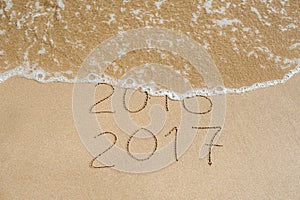 New Year 2017 is coming concept - inscription 2016 and 2017 on a beach sand, the wave is almost covering the digits 2016