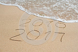 New Year 2017 is coming concept - inscription 2016 and 2017 on a beach sand, the wave is almost covering the digits 2016