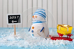 New Year 2017 is coming concept. Snowman with red sled stand near written on direction sign.