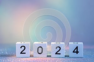 2024 New Year Coming. White Wooden Blocks With 2024 Number On Glitter Texture In Neon Light