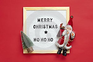 New Year composition of Santa Claus, tree, white felt board with text Merry Christmas, ho ho ho on red background Holiday card