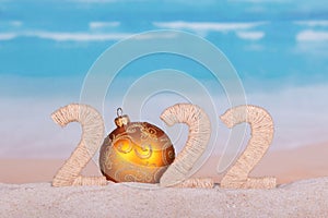 New Year concept. Lettering 2022 with bright christmas ball on beach by sea