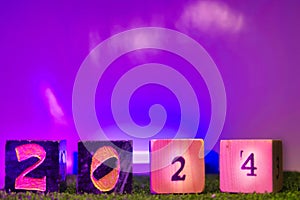 New year concept, numbers placed on wooden blocks on the green grass This picture has purple lights
