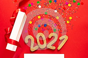 New Year concept. Shiny golden numbers 2021 from a gift box and colorful confetti on a red paper background. Gift, surprise,