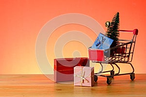 NEW YEAR CONCEPTUAL with shopping trolley,gift boxes and Christmas tree on a wooden table