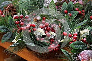 New year decor from red berries and green leaves of coniferous branches under artificial snow in a basket on the table