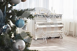 New Year decoration. Christmas tree near white piano at the window background