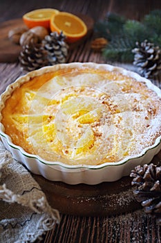 New Year dessert. Orange clafoutis with praline, powdered sugar dressing, spruce branch and pine cones decoration