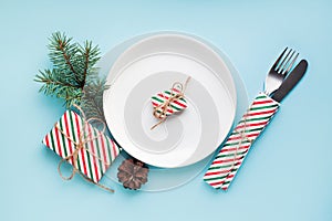 New year dinner table place setting with plate, present box, christmas eve fir branch on red background. Minimal frame