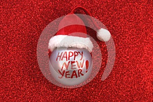 New year eve concept. Christmas ball bauble with text happy new year on red glitter background.