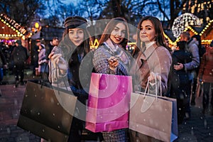 New Year concept. Women friends burning sparklers in Lviv by Christmas tree on street fair. Girls holding shopping bags