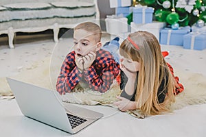 Warm photo of pretty siblings watching new year movie while laying on the carpet under Christmas fir.