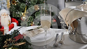 New Year holiday. Champagne being poured into glass on decorated feast table and Christmas tree with colorful twinkle