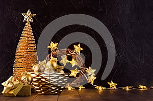 New Year home decor in dark and golden color - Christmas trees, glowing lights, stars, balls, gift box, ribbons in black interior.