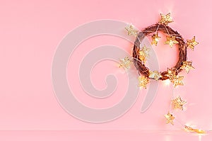 New Year home decoration - glowing gold lights with stars in wreath in soft light pink interior, copy space.