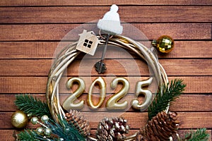 New Year House key with keychain cottage on festive brown wooden background with number 2025 in wreath, lights of garlands.