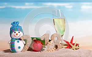New Year inscription 2018, ball instead number 0, bottle and glass champagne, snowman, Christmas tree, starfish in sand.