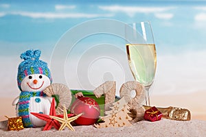New Year inscription 2018, bottle and glass of champagne, snowman, gifts, Christmas ball and starfish in sand on beach.
