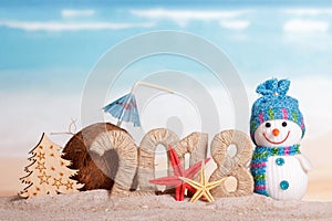 New Year inscription 2018, coconut with drinking straw and umbrella, the snowman and Christmas tree, starfish on sand.