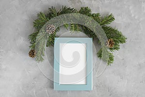 New year mockup: christmas tree branches with blue photo frame on grey background. Holidays concept