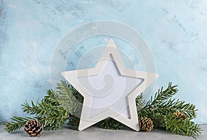 New year mockup: christmas tree branches with white star shaped photo frame on blue background. Holidays concept. Text space, copy