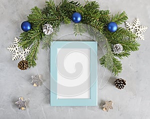 New year mockup: decorated christmas tree branches with blue photo frame on grey background. Holidays concept