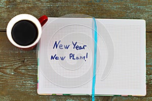 `New year, new plan` text on notepad , with cup of coffee and pen on the wooden table - business and finance concept