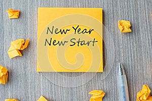 NEW YEAR NEW START word on yellow note with pen and crumbled paper on wooden table background. Resolutions, Strategy and Goal