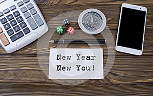 New Year New You written on paper, wooden background desk with calculator, dice, compass, smart phone and pen.